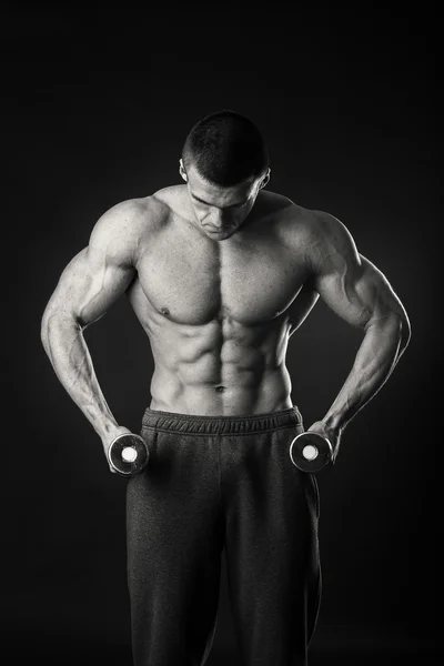 Muscular man takes exercises with dumbbells on a dark background — Stock Photo, Image