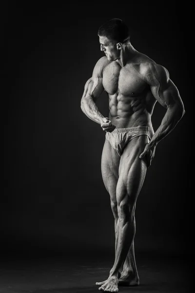 Bodybuilder professionista mostra il suo corpo su uno sfondo scuro — Foto Stock