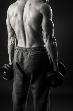 Kaslı adam egzersizleri dumbbells ile karanlık bir arka plan üzerine alır.