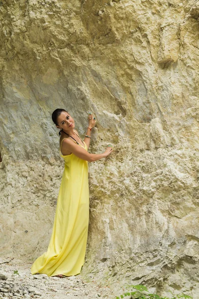 Krásná brunetka v žlutých šatech na pozadí Rock — Stock fotografie