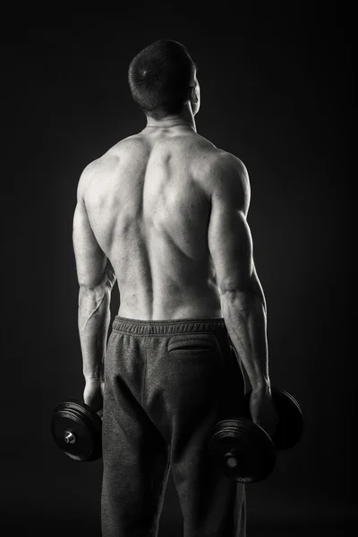 Homem muscular faz exercícios com halteres em um fundo escuro — Fotografia de Stock