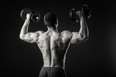 Kaslı adam egzersizleri dumbbells ile karanlık bir arka plan üzerine alır.