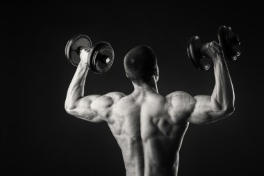 Kaslı adam egzersizleri dumbbells ile karanlık bir arka plan üzerine alır.