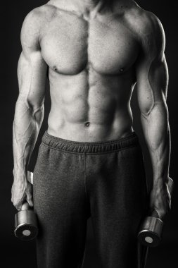 Kaslı adam egzersizleri dumbbells ile karanlık bir arka plan üzerine alır.