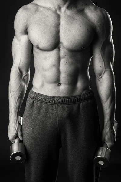 Homem muscular faz exercícios com halteres em um fundo escuro — Fotografia de Stock