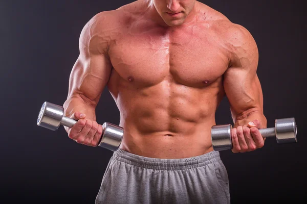 Musclé homme prend des exercices avec haltères sur un fond sombre — Photo