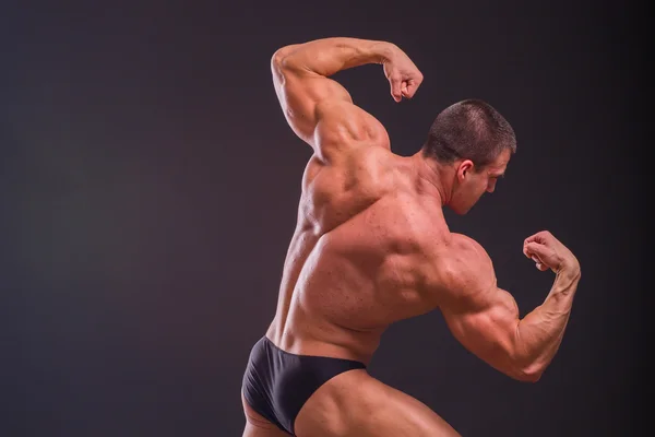 Bodybuilder professionnel montre son corps sur un fond sombre — Photo