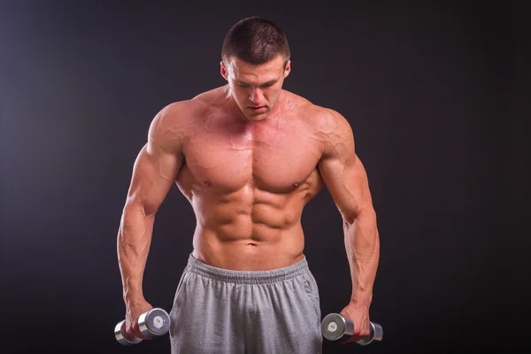 Muscular man takes exercises with dumbbells on a dark background — Stock Photo, Image
