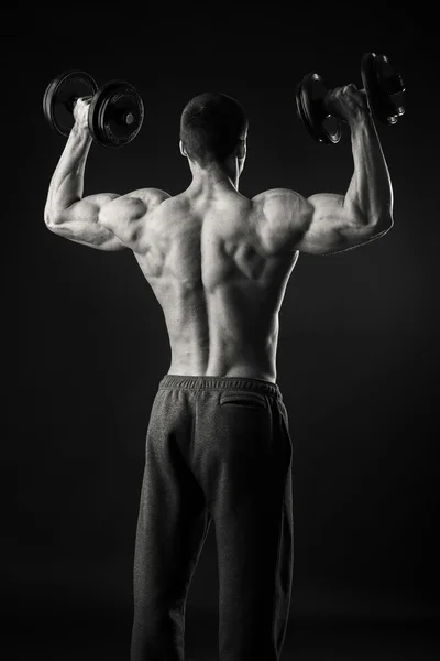 Uomo muscolare prende esercizi con manubri su uno sfondo scuro — Foto Stock