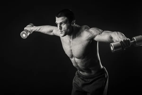 Homem muscular faz exercícios com halteres em um fundo escuro — Fotografia de Stock