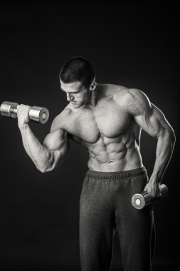 Kaslı adam egzersizleri dumbbells ile karanlık bir arka plan üzerine alır.