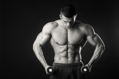 Kaslı adam egzersizleri dumbbells ile karanlık bir arka plan üzerine alır.