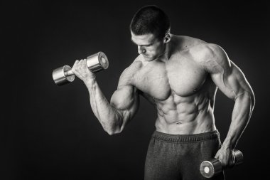 Kaslı adam egzersizleri dumbbells ile karanlık bir arka plan üzerine alır.