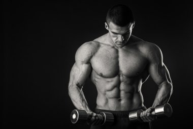 Kaslı adam egzersizleri dumbbells ile karanlık bir arka plan üzerine alır.