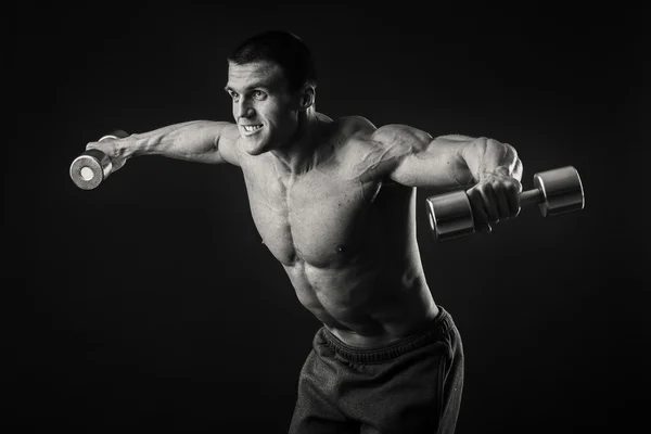 Musclé homme prend des exercices avec haltères sur un fond sombre — Photo