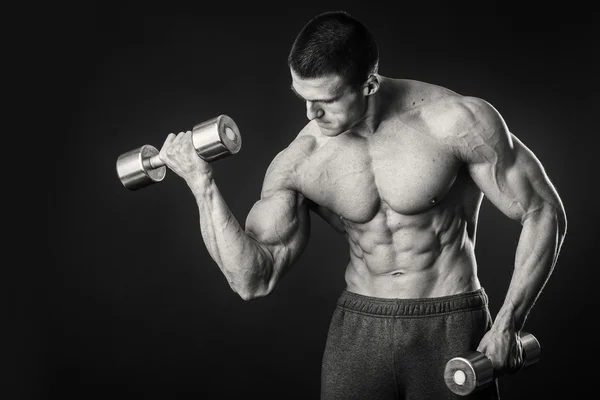 Homem muscular faz exercícios com halteres em um fundo escuro — Fotografia de Stock