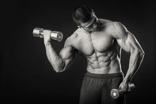 Kaslı adam egzersizleri dumbbells ile karanlık bir arka plan üzerine alır. — Stok fotoğraf