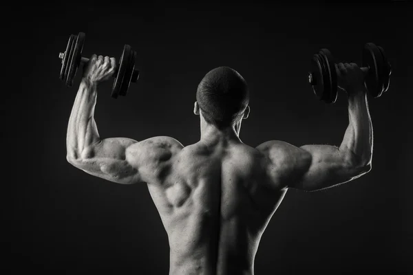 Muscular hombre toma ejercicios con mancuernas sobre un fondo oscuro —  Fotos de Stock