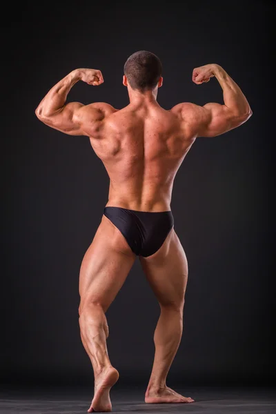 Professional bodybuilder shows his body on a dark background — Stock Photo, Image