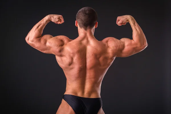 Profi-Bodybuilder zeigt seinen Körper auf dunklem Hintergrund — Stockfoto