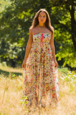 Young beautiful brunette in a dress middle of the park on a warm summer day