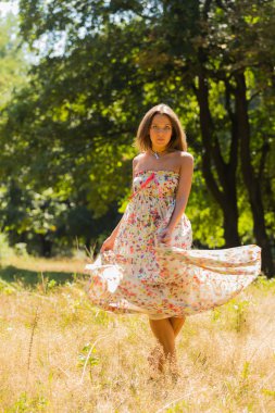 Young beautiful brunette in a dress middle of the park on a warm summer day