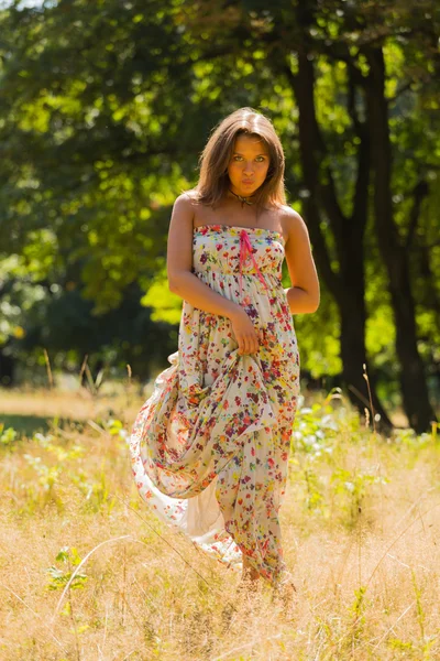 Young beautiful brunette in a dress middle of the park on a warm summer day — Stok fotoğraf