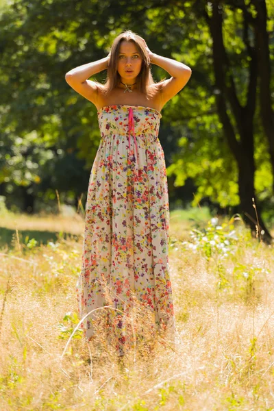 Jovem morena bonita em um vestido no meio do parque em um dia quente de verão — Fotografia de Stock