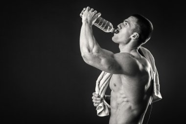 Muscular man on a dark background drinking water after workout clipart
