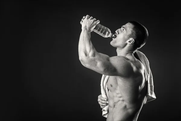 Uomo muscolare su uno sfondo scuro acqua potabile dopo l'allenamento — Foto Stock