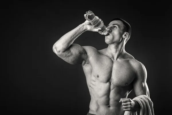 Svalnatý muž na tmavém pozadí pitné vody po cvičení — Stock fotografie
