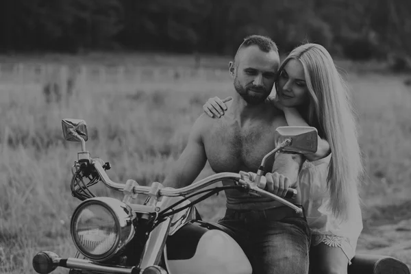 Uomo muscolare con una bella donna su una moto nel mezzo di una strada di campo — Foto Stock
