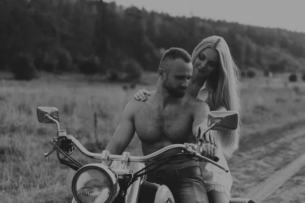 Homem musculoso com uma mulher bonita em uma motocicleta no meio de uma estrada de campo — Fotografia de Stock