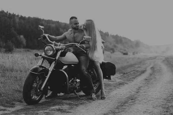 Muscular man with a beautiful woman on a motorcycle middle of a field road