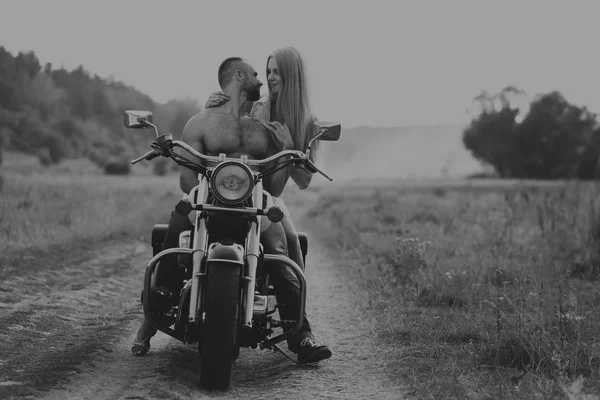 Hombre musculoso con una mujer hermosa en una motocicleta en medio de un camino de campo —  Fotos de Stock