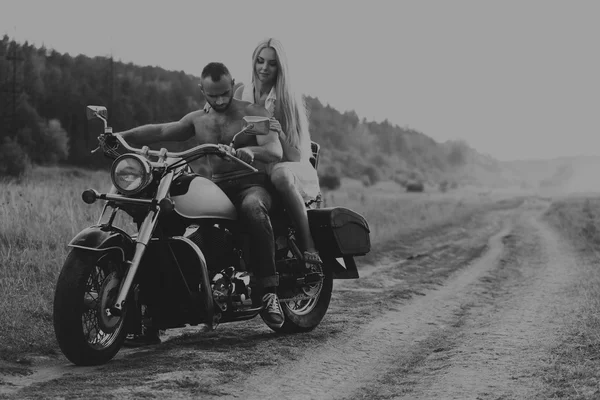 Muskulöser Mann mit einer schönen Frau auf einem Motorrad mitten auf einem Feldweg — Stockfoto