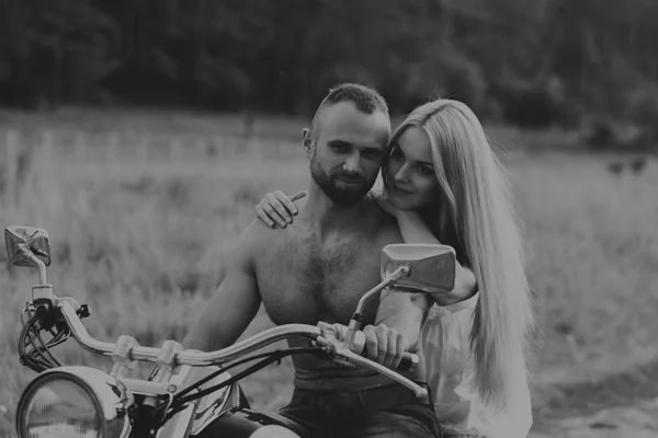 Uomo muscolare con una bella donna su una moto nel mezzo di una strada di campo — Foto Stock