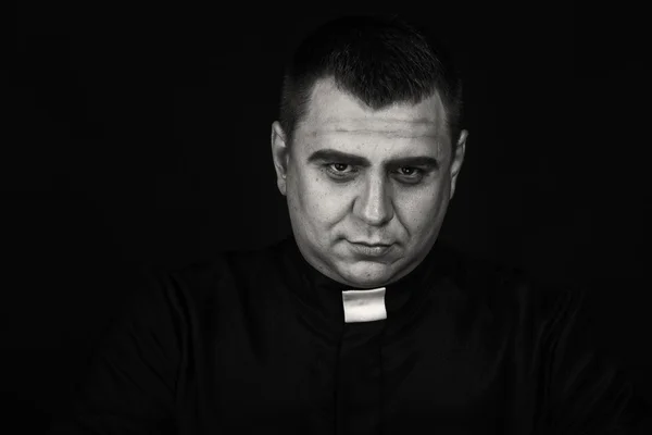 A professional stage actor in the guise of a priest against a dark background