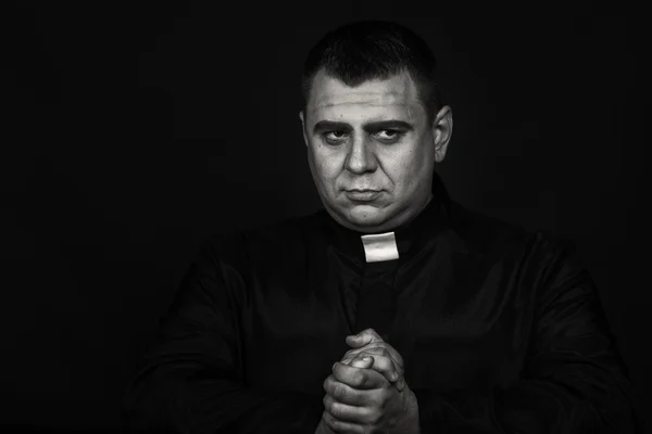 A professional stage actor in the guise of a priest against a dark background