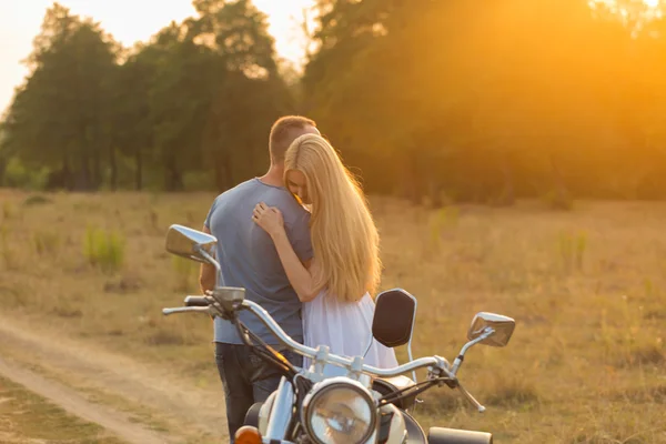 Gespierde man met een mooie vrouw op een motorfiets midden van een veld weg — Stockfoto
