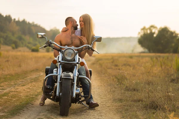 Homem musculoso com uma mulher bonita em uma motocicleta no meio de uma estrada de campo — Fotografia de Stock