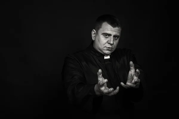 A professional stage actor in the guise of a priest against a dark background