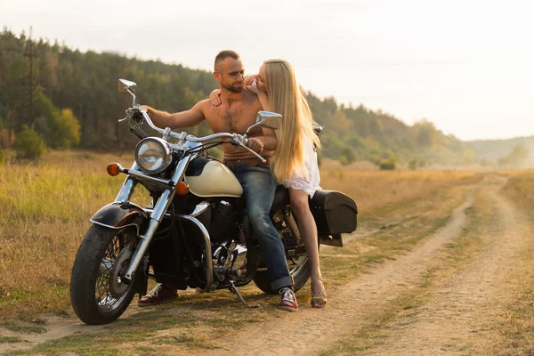 Homme musclé avec une belle femme sur une moto au milieu d'une route de champ — Photo