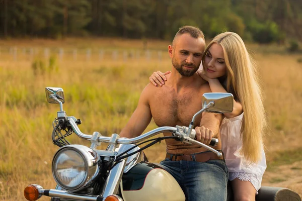 Gespierde man met een mooie vrouw op een motorfiets midden van een veld weg — Stockfoto