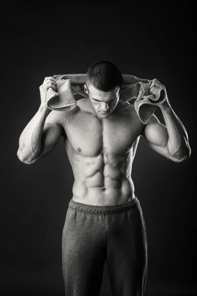 Homem musculoso com uma toalha nas mãos sobre um fundo escuro — Fotografia de Stock