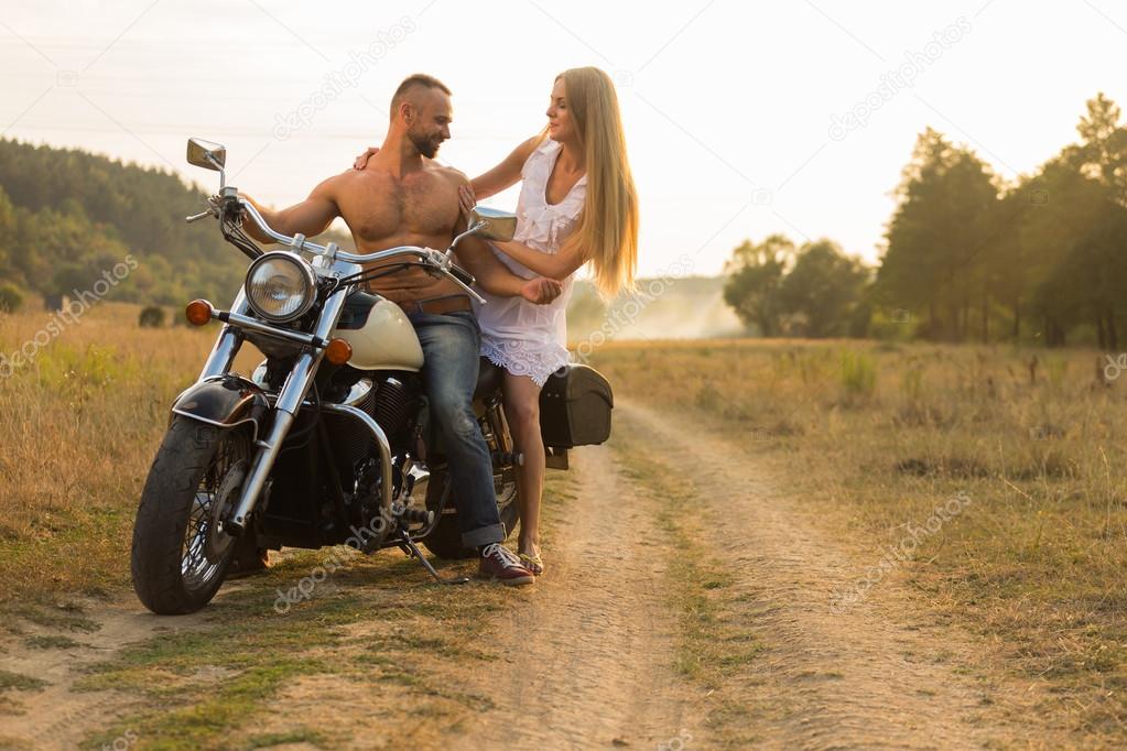 Muscular man with a beautiful woman on a motorcycle middle of a field road