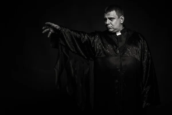 Un actor teatral profesional disfrazado de sacerdote sobre un fondo oscuro — Foto de Stock