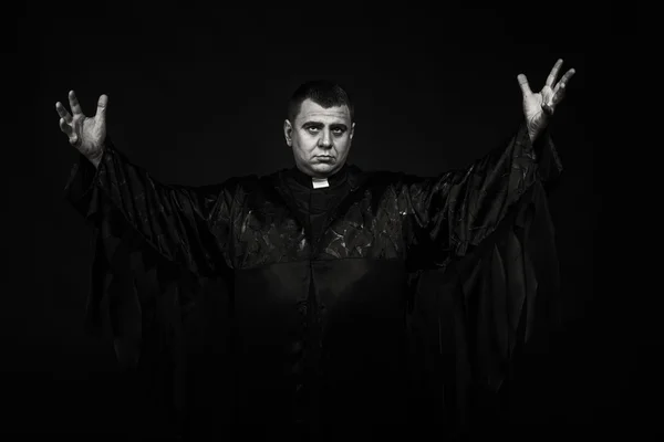 A professional stage actor in the guise of a priest against a dark background