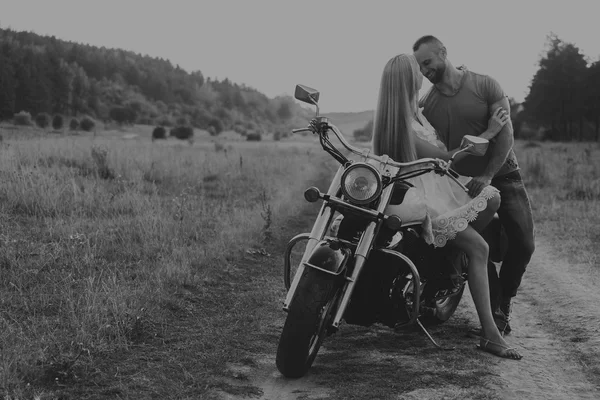 Homme musclé avec une belle femme sur une moto au milieu d'une route de champ — Photo