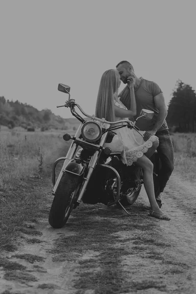Muskulöser Mann mit einer schönen Frau auf einem Motorrad mitten auf einem Feldweg — Stockfoto